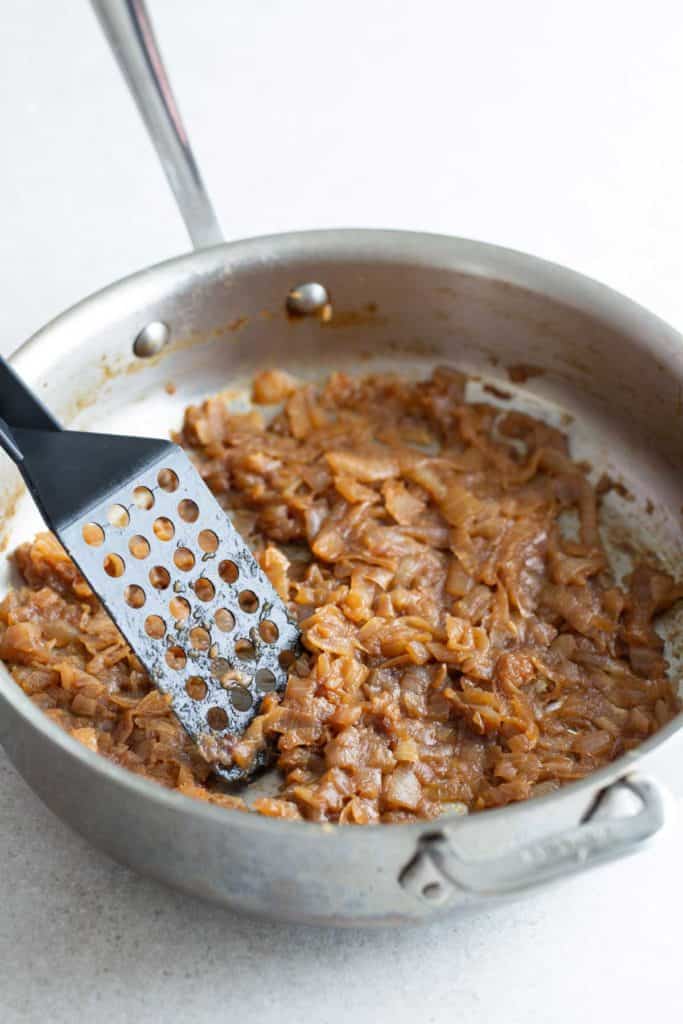 Sautéed onions in a frying pan with a spatula.
