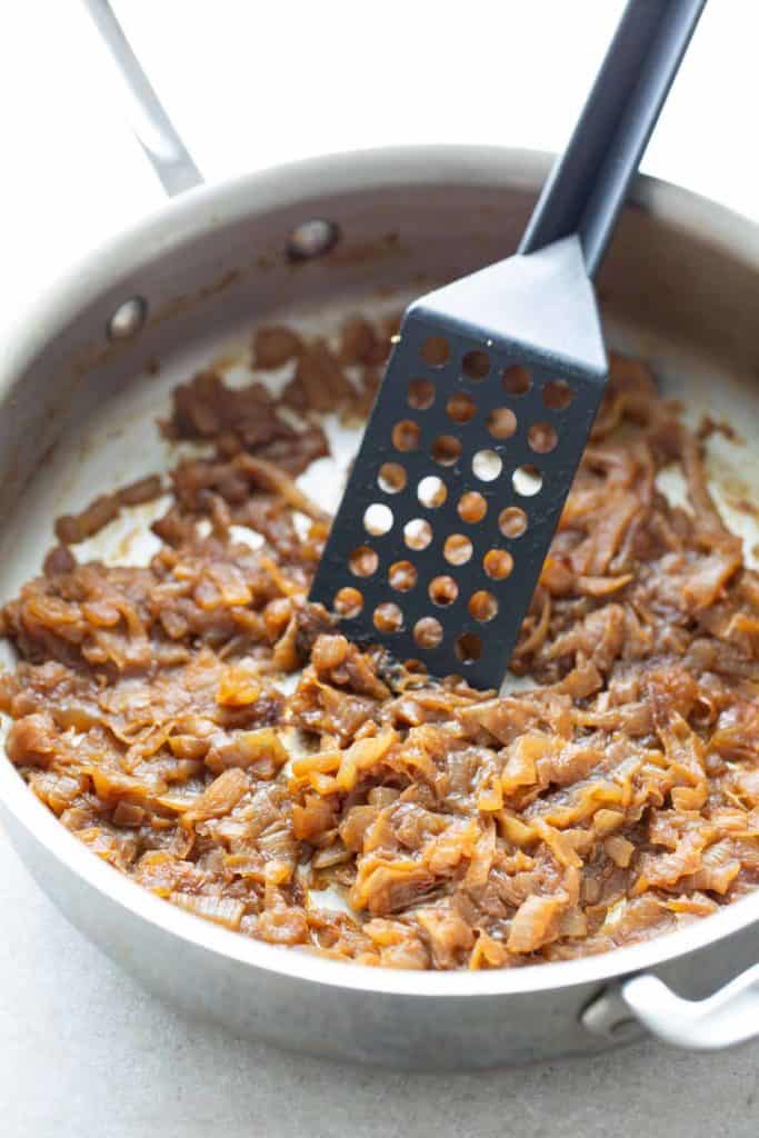 Pan-fried caramelized onions with a spatula on a stovetop.