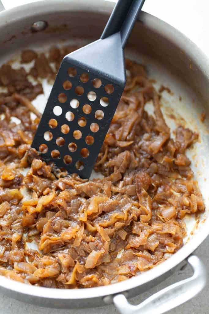 Caramelized onions in a pan with a spatula.