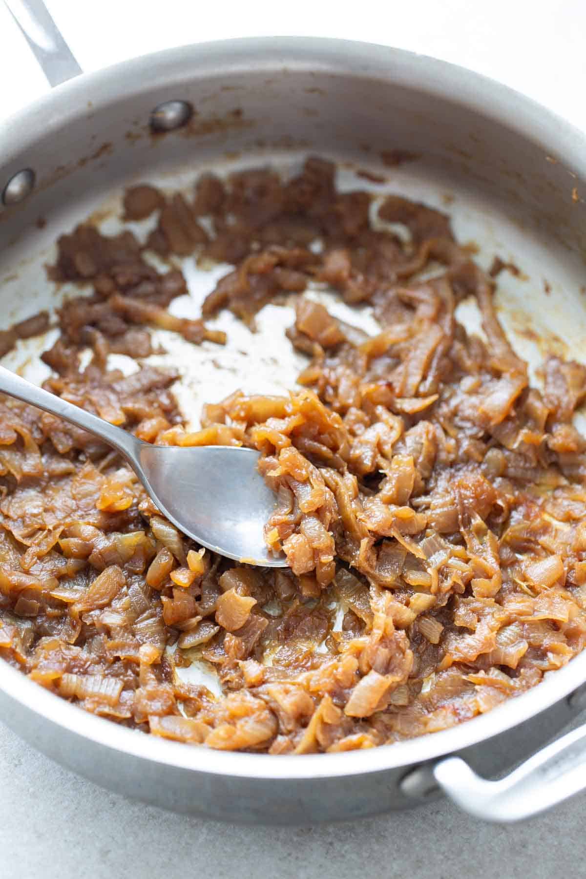 Caramelized onions in a pan with a spoon.