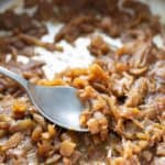 Caramelized onions in a pan with a spoon.