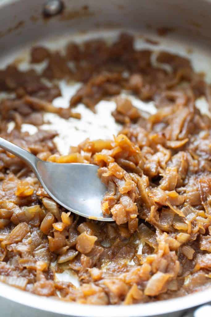 How to Caramelize Onions Caramelized onions in a pan with a spoon.