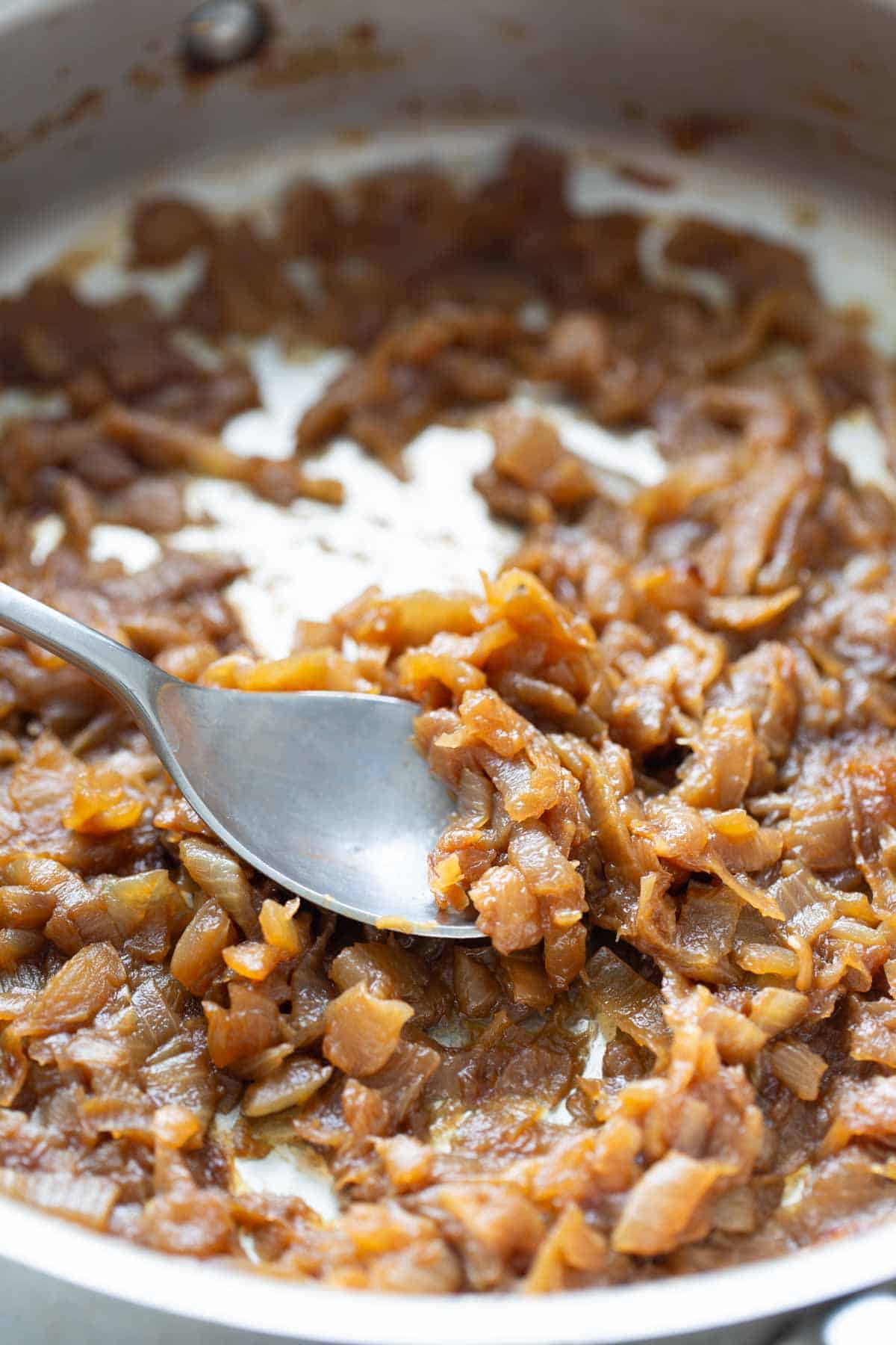 Caramelized onions in a pan with a spoon.