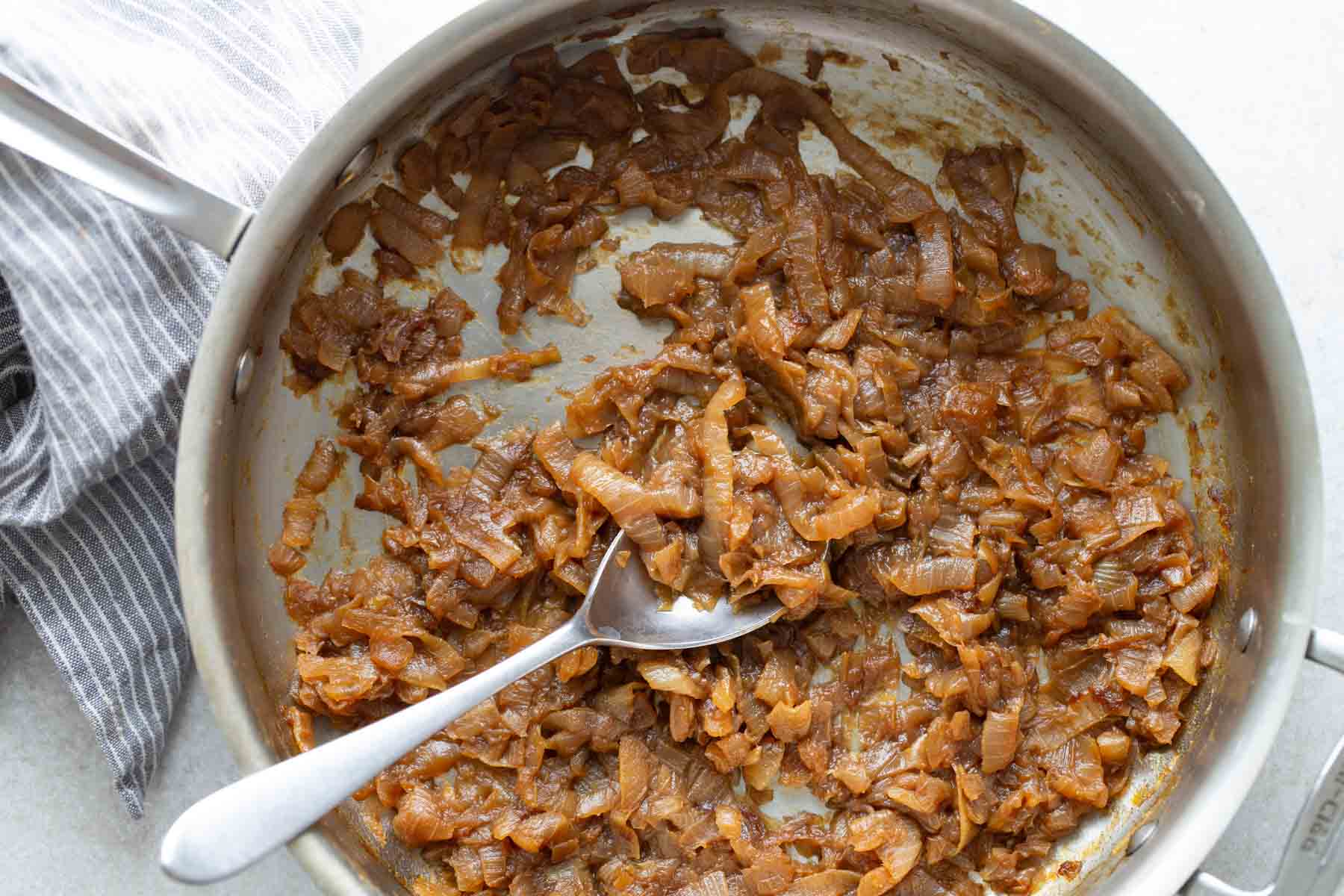 Caramelized onions in a frying pan with a spoon.