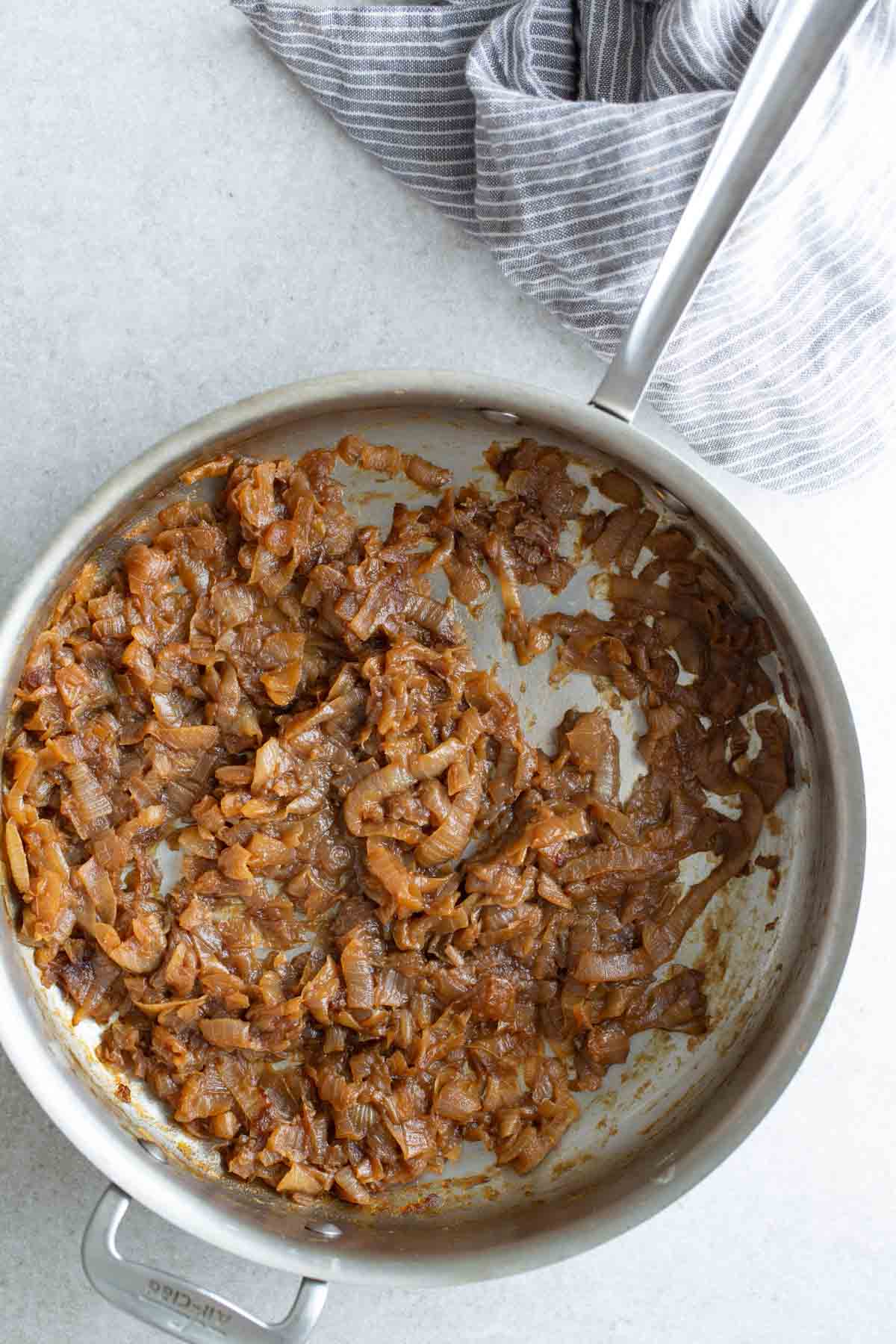 Caramelized onions in a stainless steel pan with a pair of tongs.