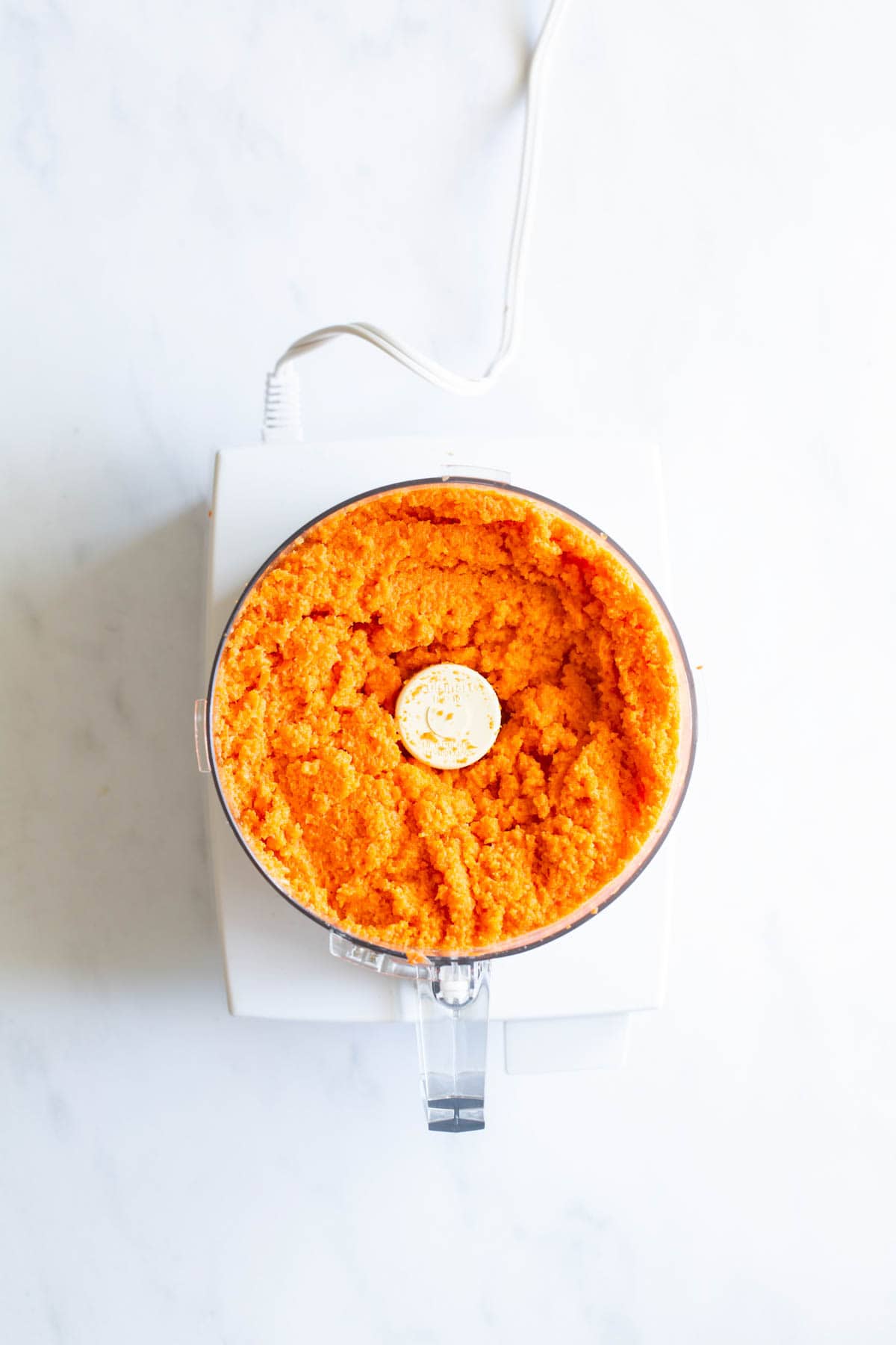 Top-down view of a food processor filled with a freshly prepared orange mixture.