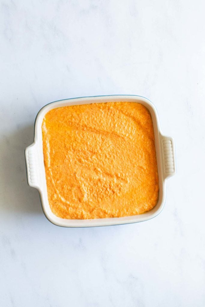 A baking dish with orange-colored batter on a white surface.