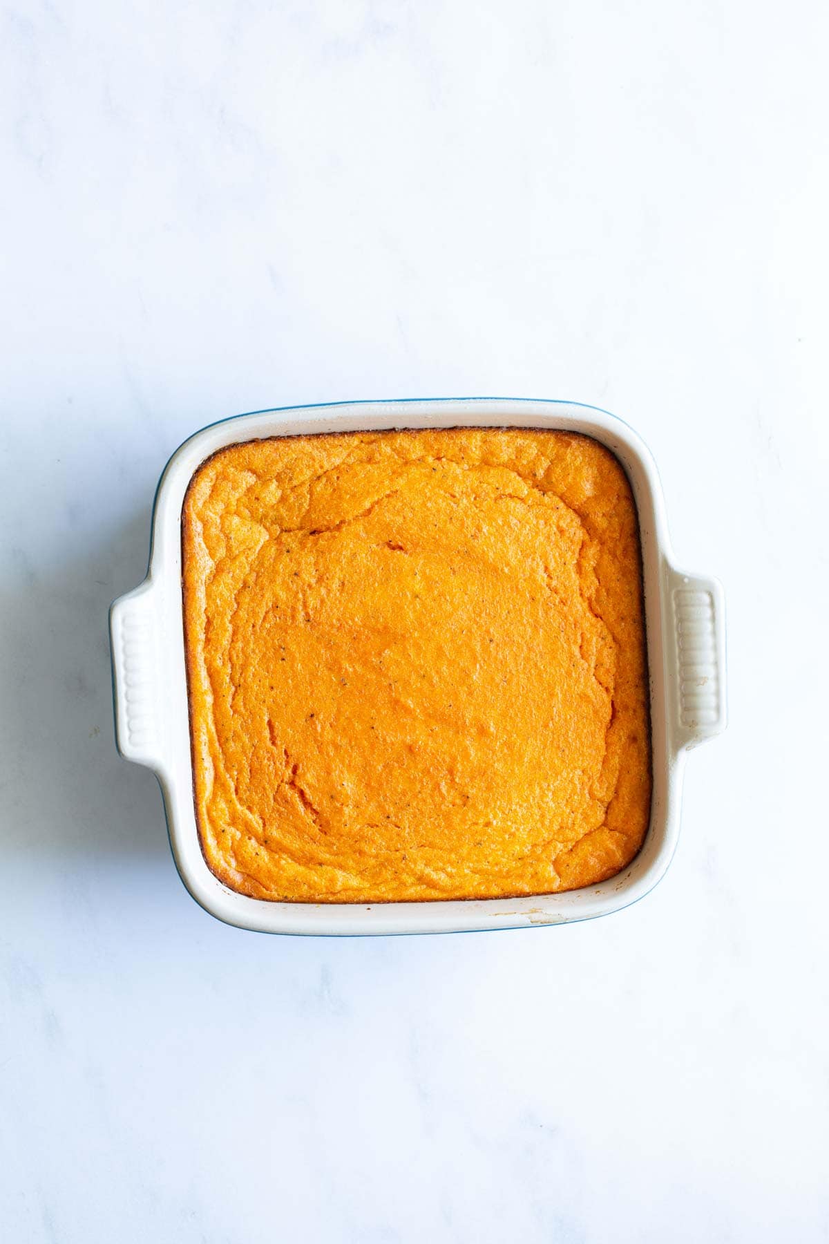 A baking dish filled with carrot souffle on a white surface.