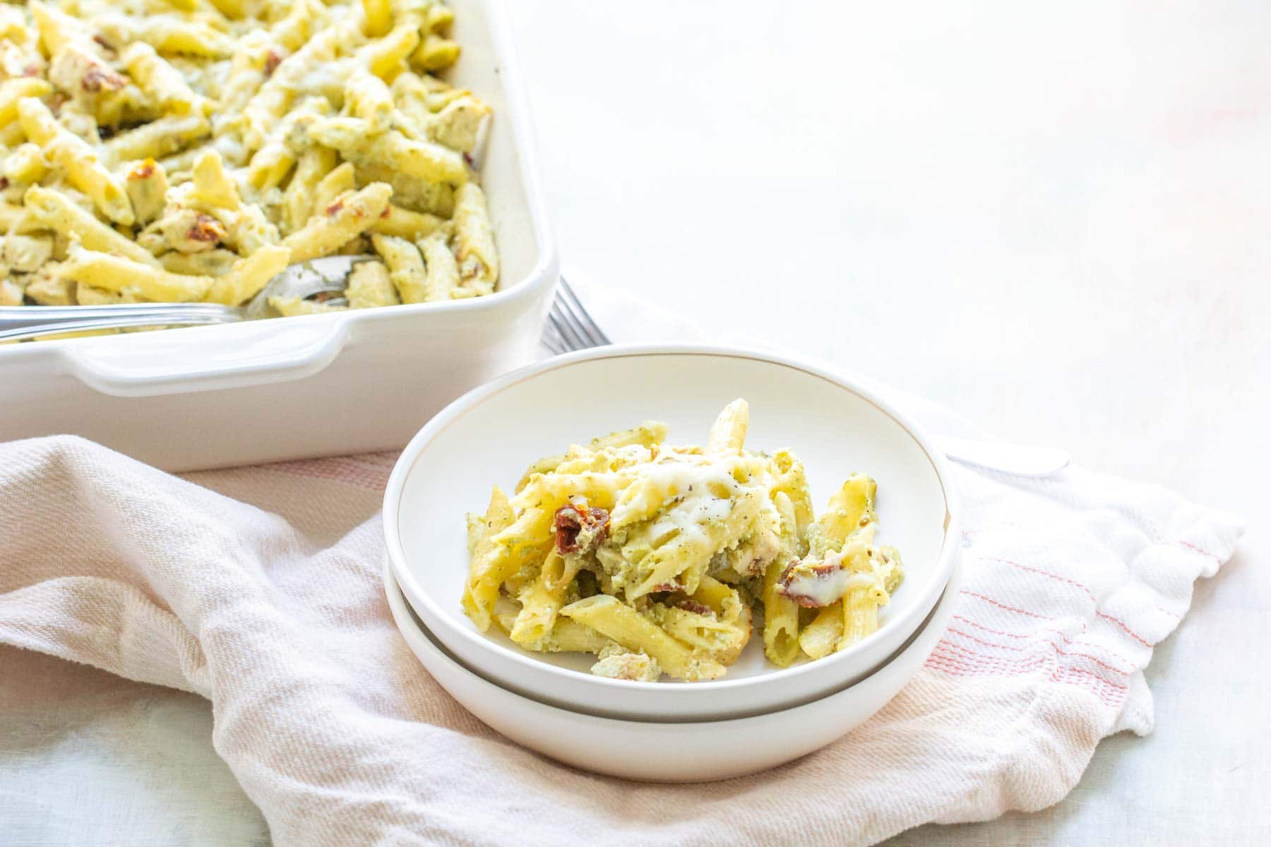 A bowl of creamy pasta salad beside a larger dish filled with more of the same salad, set on a white background.