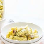 A bowl of pasta salad with creamy dressing on a white tablecloth, with a serving dish in the background.