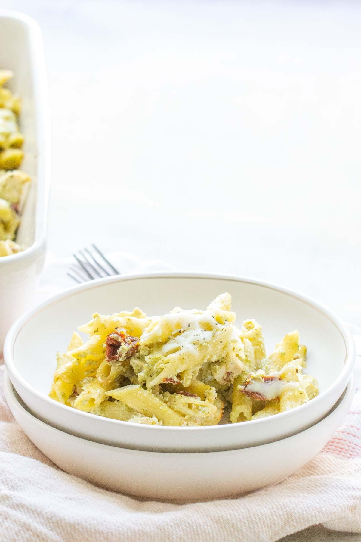 A bowl of pasta salad with creamy dressing on a white tablecloth, with a serving dish in the background.