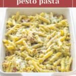 A white baking dish filled with chicken pesto pasta, featuring baked penne mixed with tender chicken, pesto sauce, sun-dried tomatoes, and melted cheese.