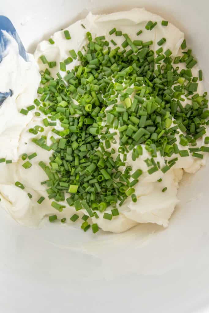 Bowl of cream cheese topped with chopped chives, with a mixing spoon.