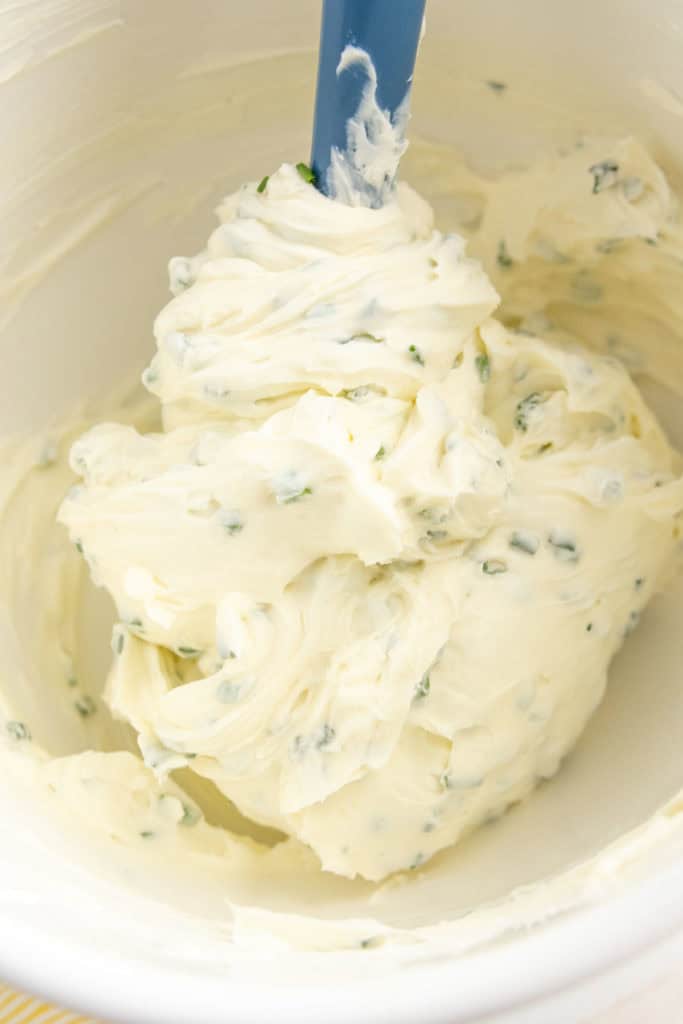 Homemade chive cream cheese in a mixing bowl with a blue spatula.