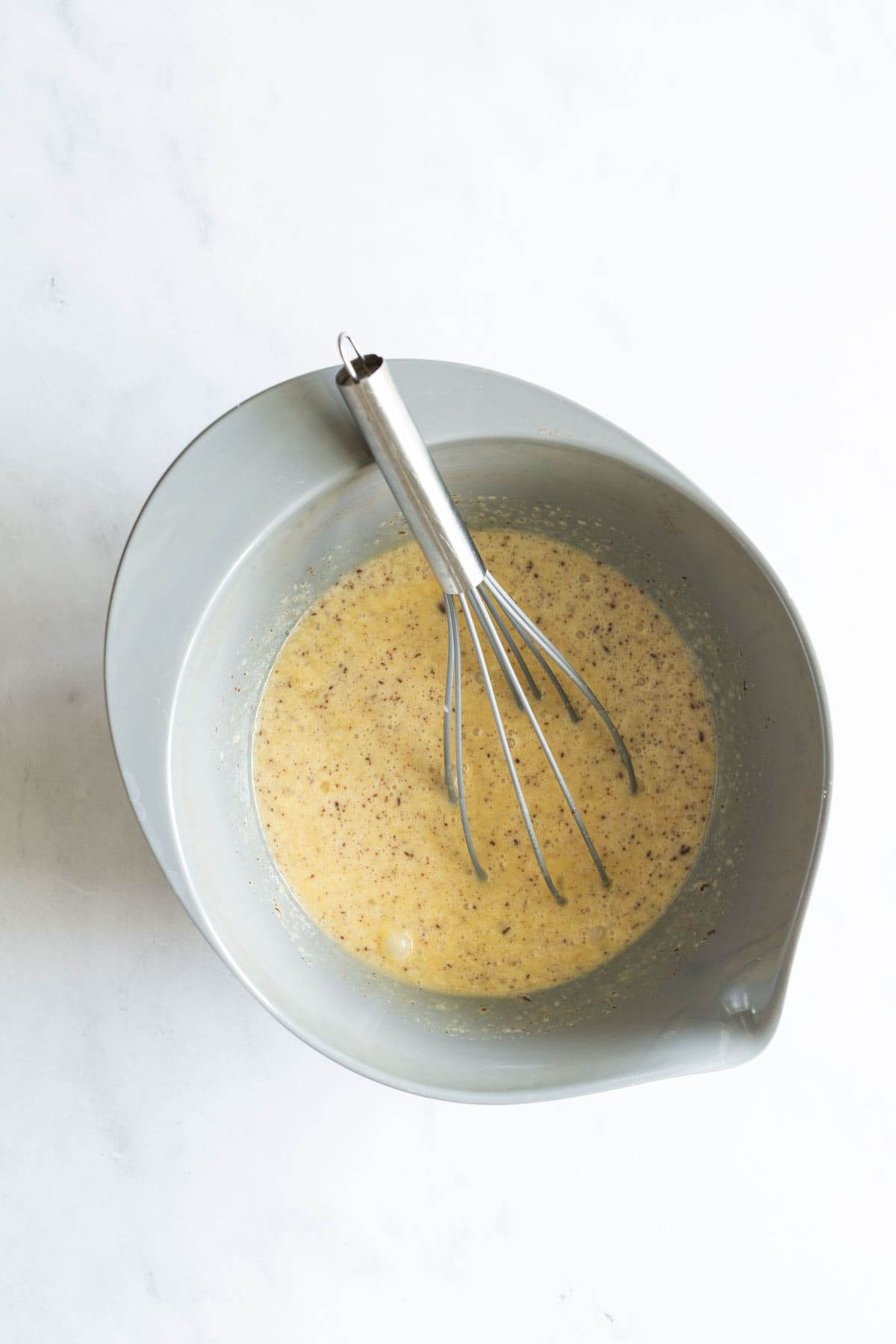 A blue bowl containing a whisk and a mixture of beaten eggs on a white surface.