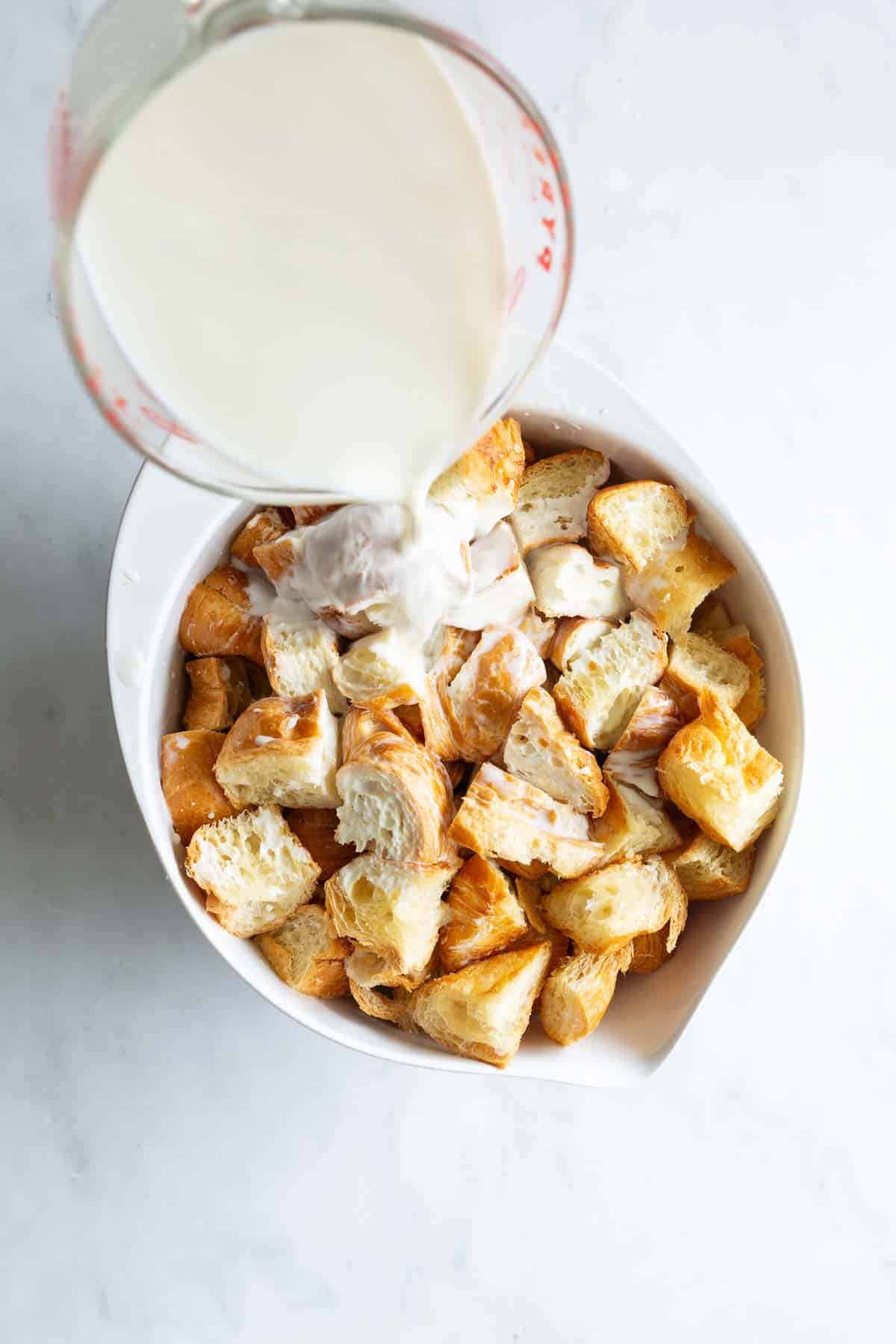 Milk being poured over a bowl of cubed croissants.