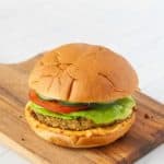 A veggie burger with lettuce, tomato, and cucumber on a cutting board.