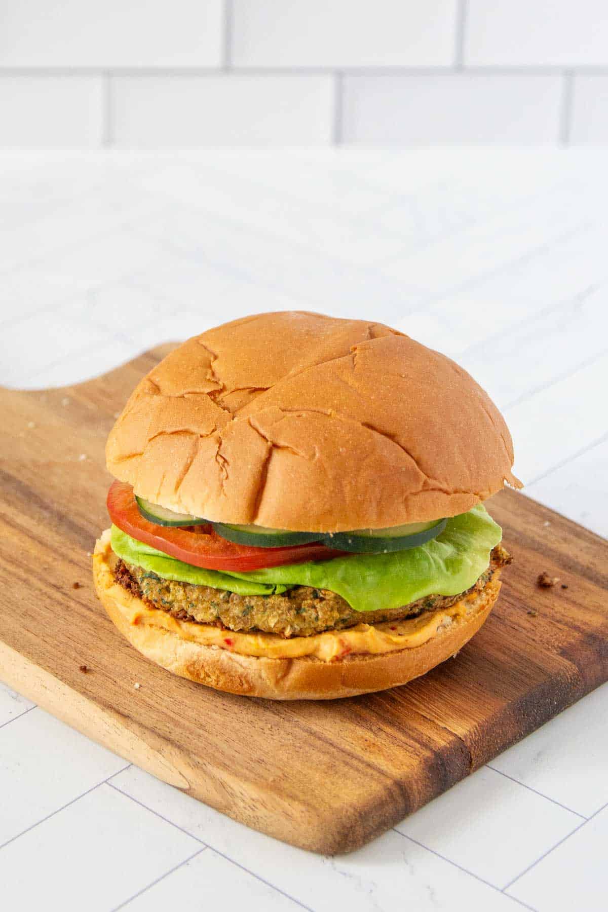 A veggie burger with lettuce, tomato, and cucumber on a cutting board.