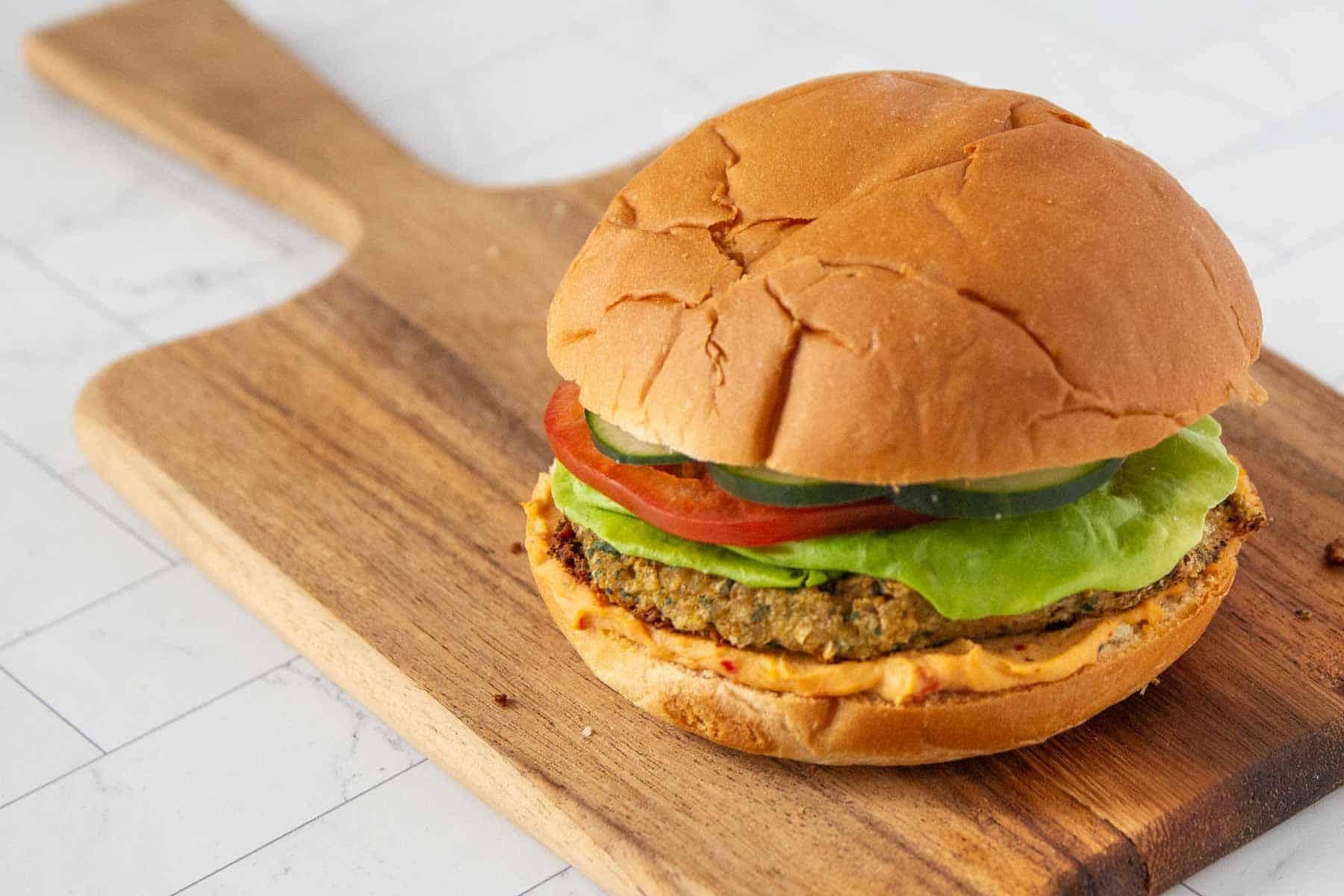 Veggie burger with lettuce, tomato, and cucumber on a wooden serving board.