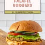 A flavorful falafel burger with lettuce, tomato, and cucumber on a bun rests on a wooden board. Text above reads "Falafel Burgers—get the recipe at stetted.com." Try these delicious homemade falafel burgers today!.