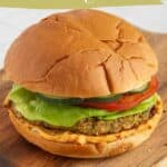 A falafel burger with lettuce, tomato, cucumber, and sauce on a bun, served on a wooden board—our zesty falafel burgers are the perfect dinner option.