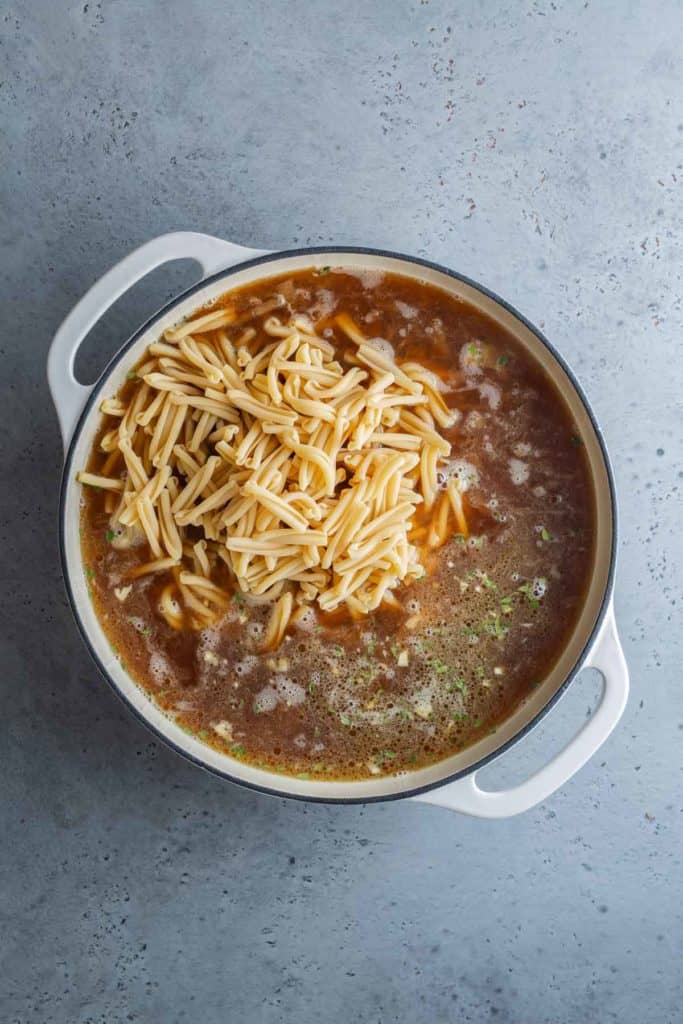 Top view of a pot filled with broth and cheddar cheese soup topped with crumbled crackers.