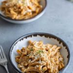 Two bowls of pasta with creamy sauce and grated cheese on top, served on a gray table with a fork on the side.