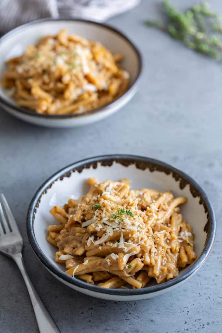 Two bowls of pasta with creamy sauce and grated cheese on top, served on a gray table with a fork on the side.