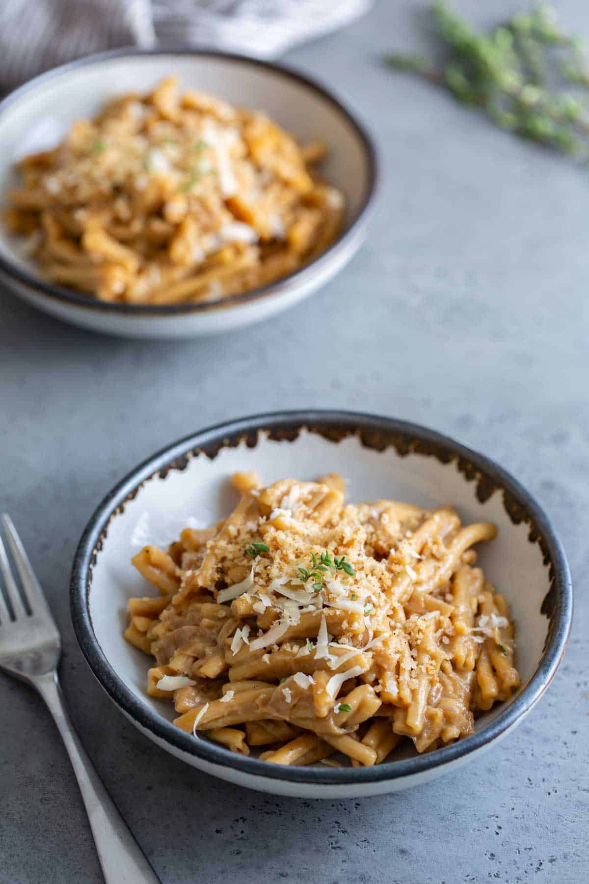 Two bowls of pasta with cheese on top.