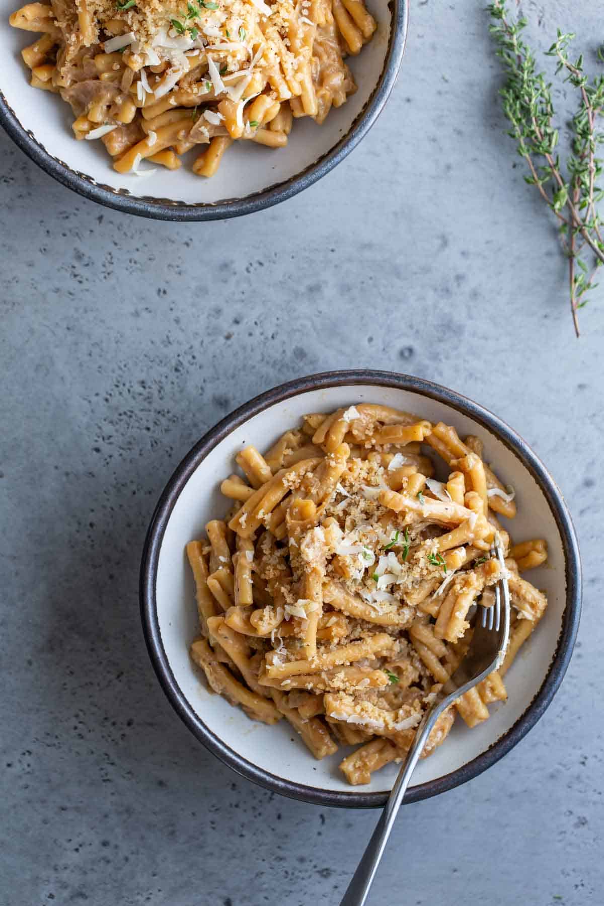 Two bowls of creamy pasta topped with grated cheese and herbs on a gray surface.