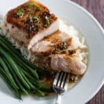 Grilled pork chop on a bed of rice with green beans, garnished with herbs, served on a white plate with a fork.