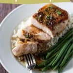 A plate with juicy honey garlic pork chops on white rice, served with green beans; one pork chop is partly sliced with a fork.