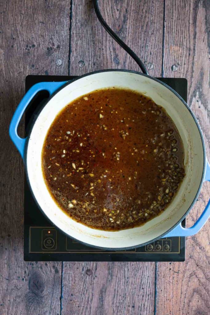 A pot of sauce cooking on an electric stove, set against a rustic wooden background.