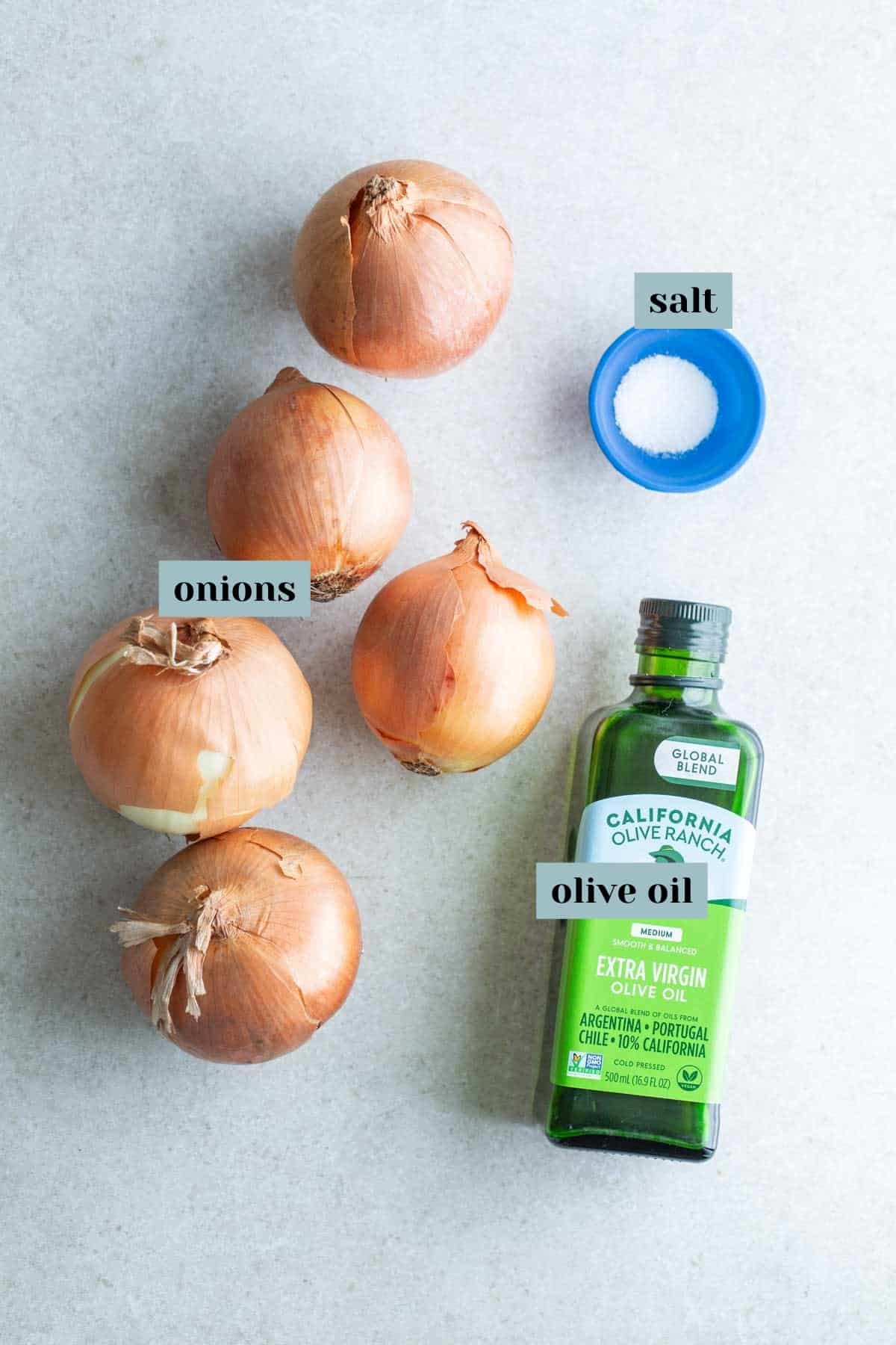 Ingredients for cooking: whole onions, olive oil, and salt on a kitchen countertop.