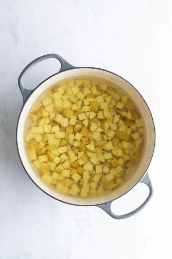 Diced potatoes soaking in water in a large pot.
