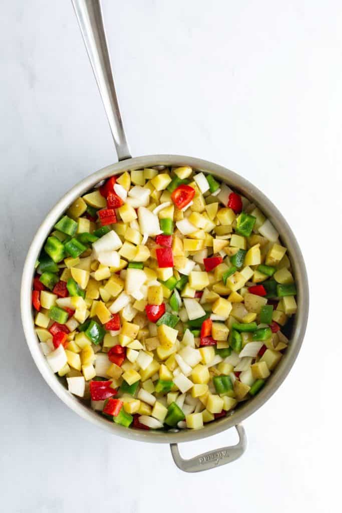 A stainless steel pan containing diced vegetables on a white surface.