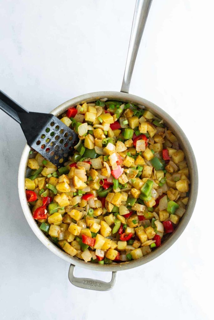 Sautéed diced vegetables in a pan with a spatula.