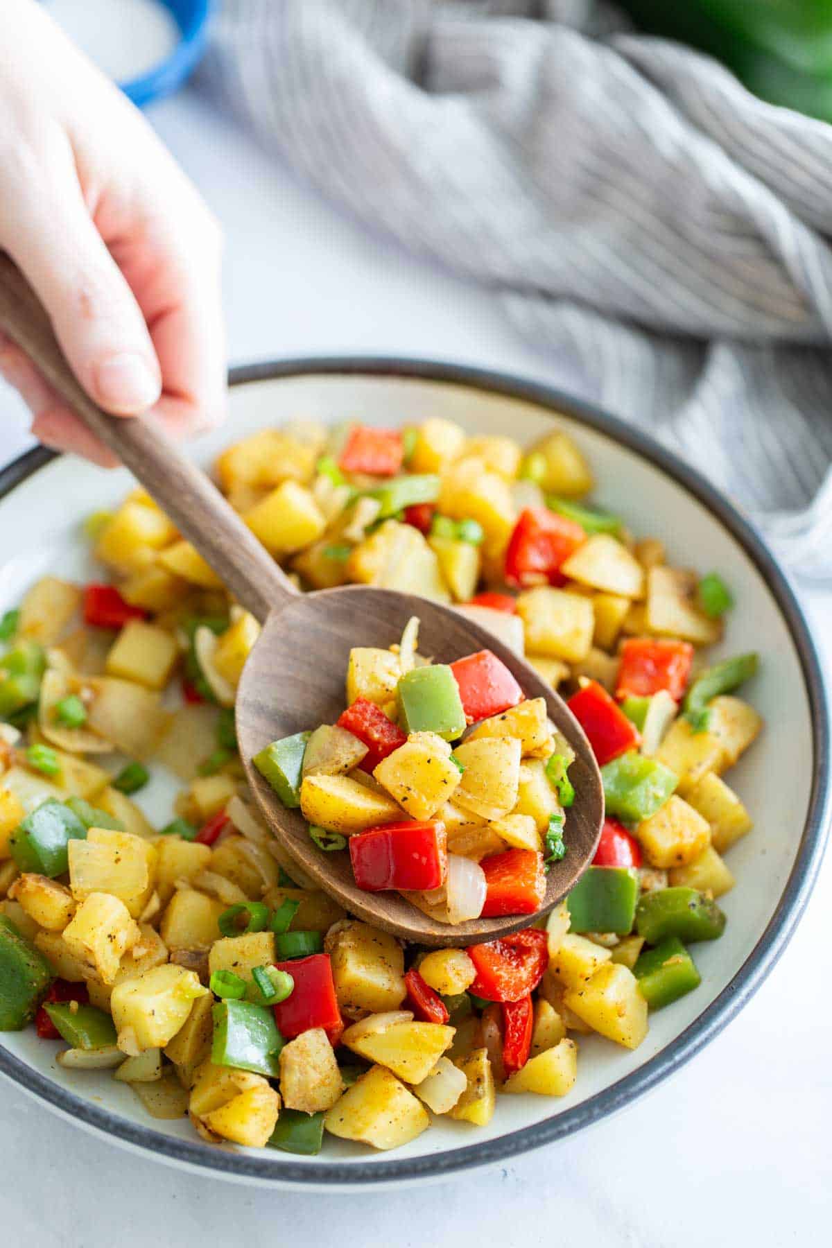 A person serving a colorful mixed vegetable sauté with a wooden spoon.