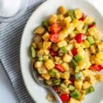 Potatoes with peppers served on a plate beside a spoon, with salt and pepper to the side.