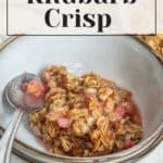 A bowl of rhubarb crisp topped with a crunchy oat layer, accompanied by a metal spoon, with text overlay reading "the ultimate rhubarb crisp recipe".