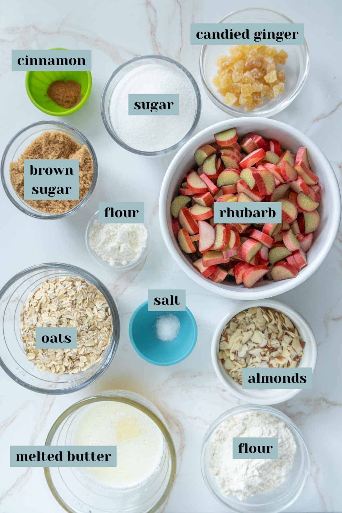 Various baking ingredients labeled in containers, including cinnamon, sugar, brown sugar, flour, oats, melted butter, salt, almonds, candied ginger, and chopped rhubarb.