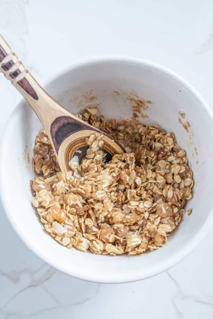 A wooden spoon mixing oatmeal with honey in a white bowl on a marble surface.