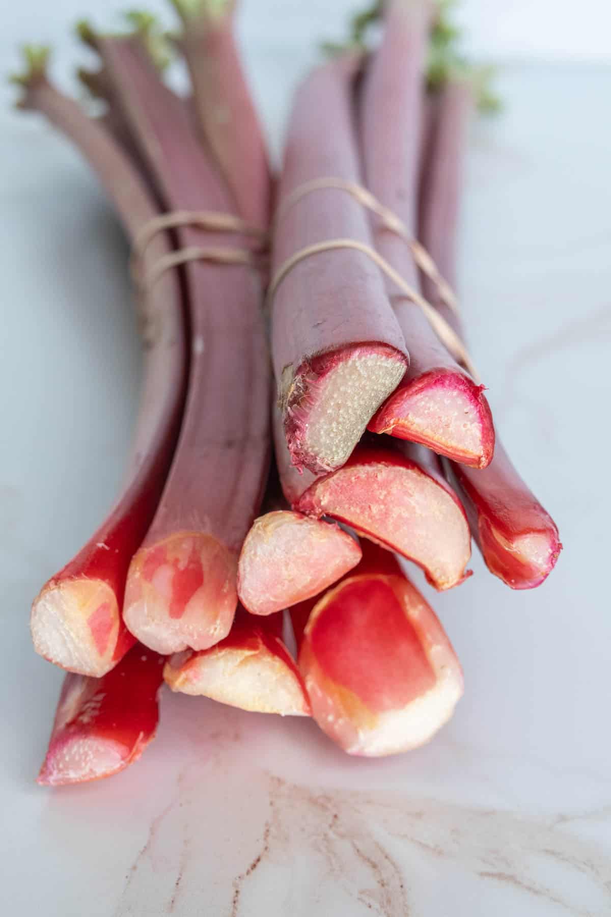 A bunch of fresh rhubarb stalks with vibrant red and green colors, bound together with twine, displayed on a marble surface.