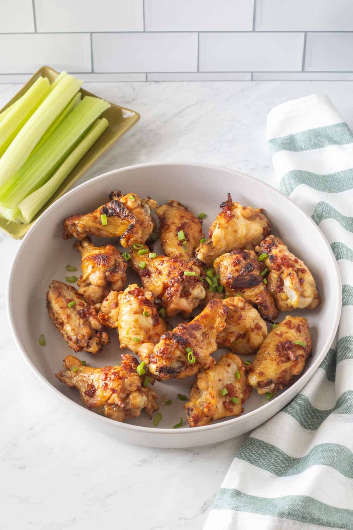 A bowl of chicken wings garnished with green onions, served with a side of celery sticks.