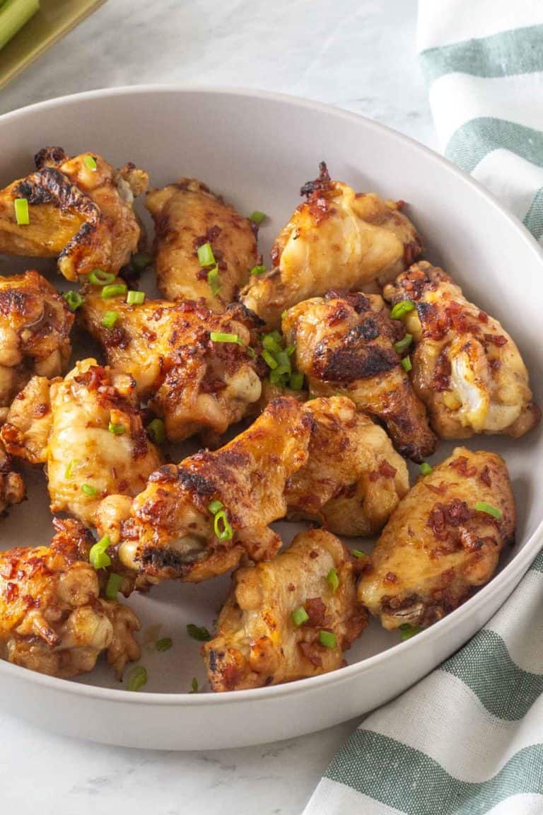 A bowl of roasted chicken wings garnished with green onions.