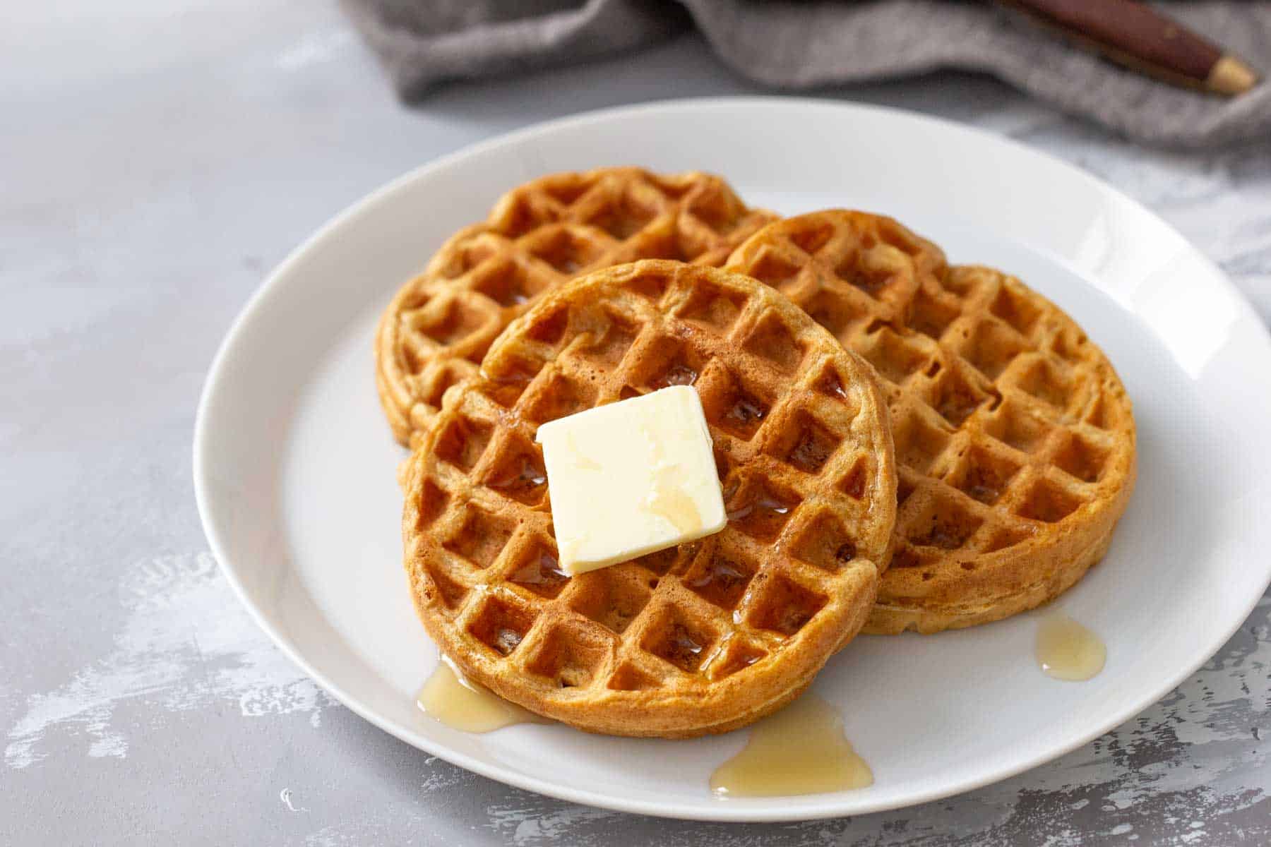 Two waffles with butter and syrup on a white plate.