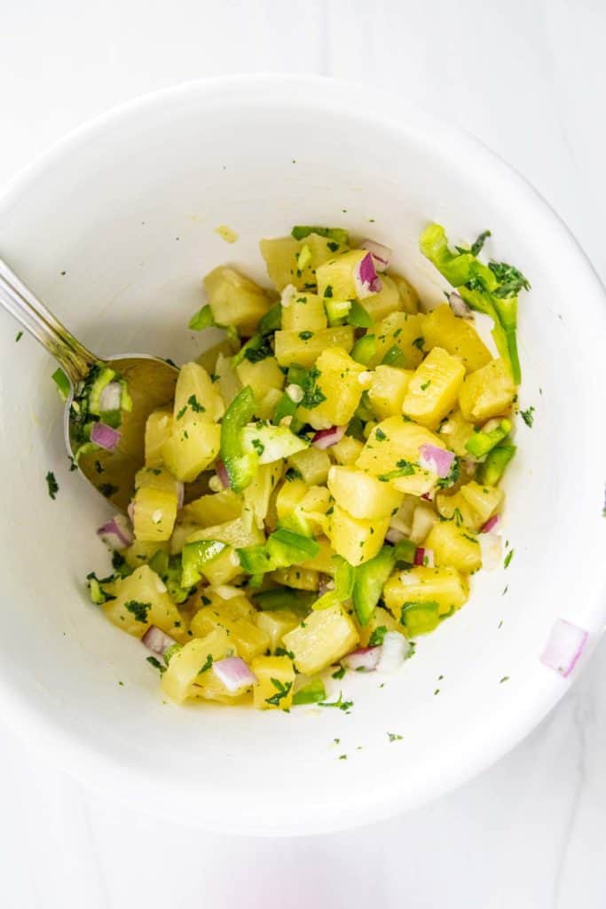 A bowl of pineapple salsa with diced jalapeno, red onion, and cilantro, mixed together, viewed from above.