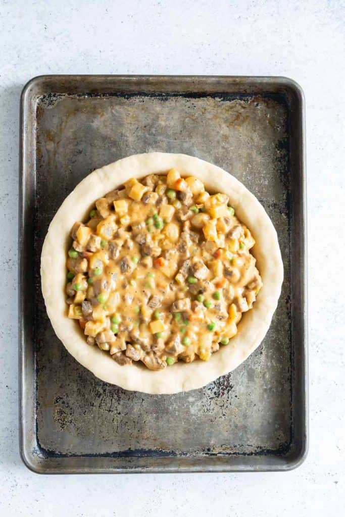 Unbaked pie filled with a mixture of ground meat and vegetables on a baking sheet, viewed from above.