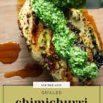 A grilled chimichurri chicken breast on a wooden board, topped with vibrant green sauce and more being spooned on, with a text overlay reading "Grilled chimichurri chicken.