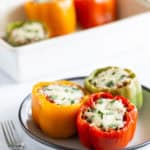 A plate of stuffed bell peppers with melted cheese, garnished with herbs, next to a baking dish with more peppers.